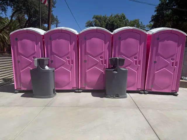 Five pink portable toilets with two gray hand-washing stations in front