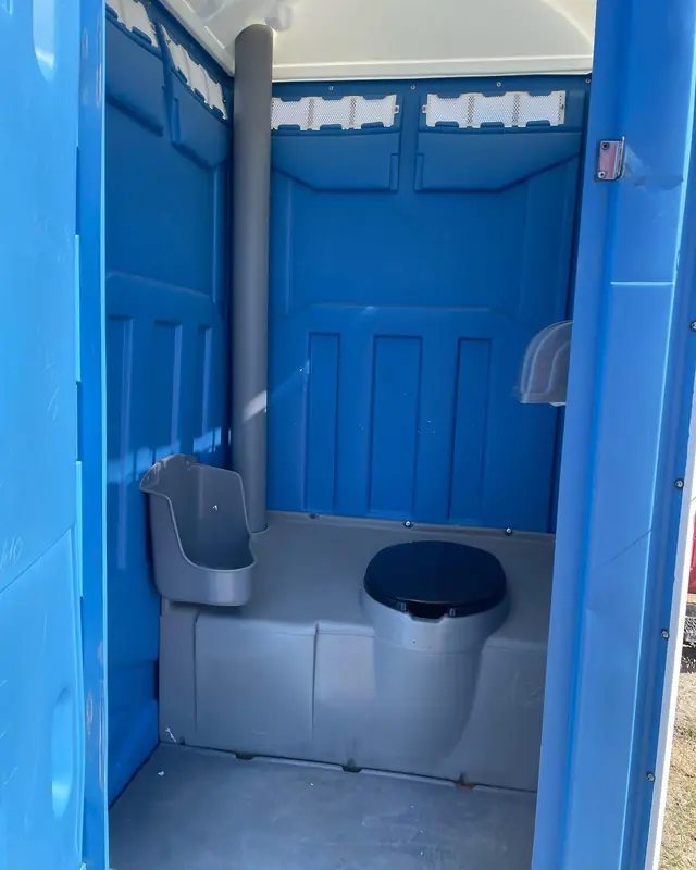 Inside a blue standard portable toilet showing the seat, urinal and vent pipe