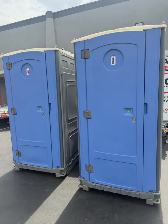 Two blue portable toilets on an open paved lot